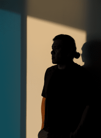 A man stands worried, his face in shadow 